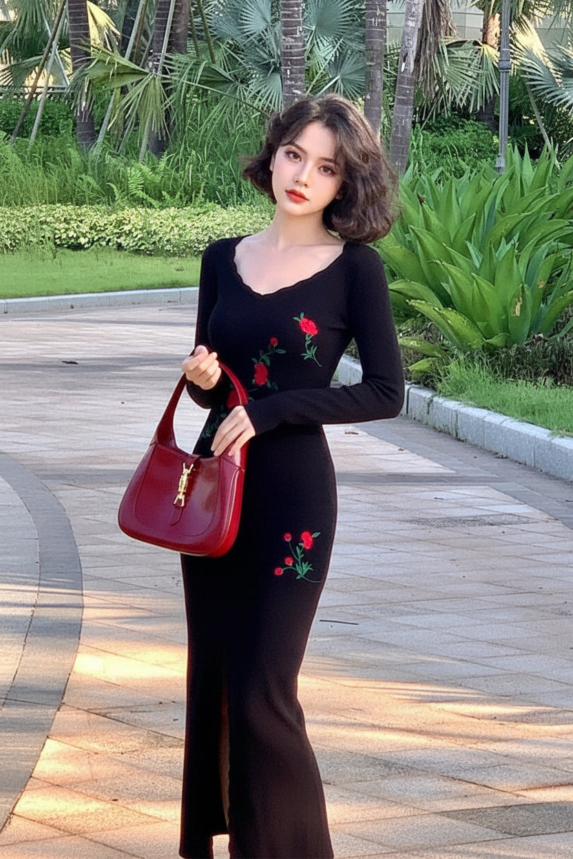Woman in a black dress with red floral embroidery holding a red handbag outdoors.