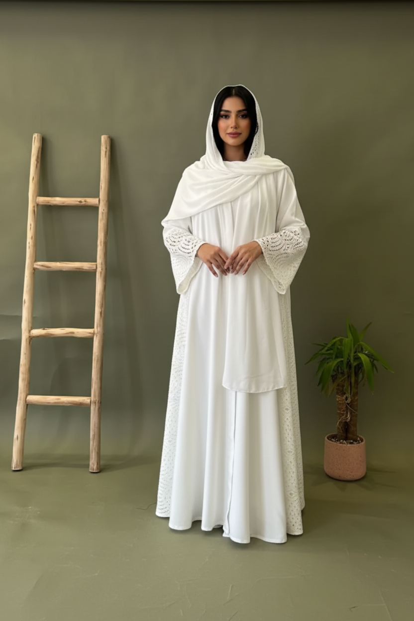 Person wearing a long, white embroidered dress standing next to a wooden ladder against a green wall.