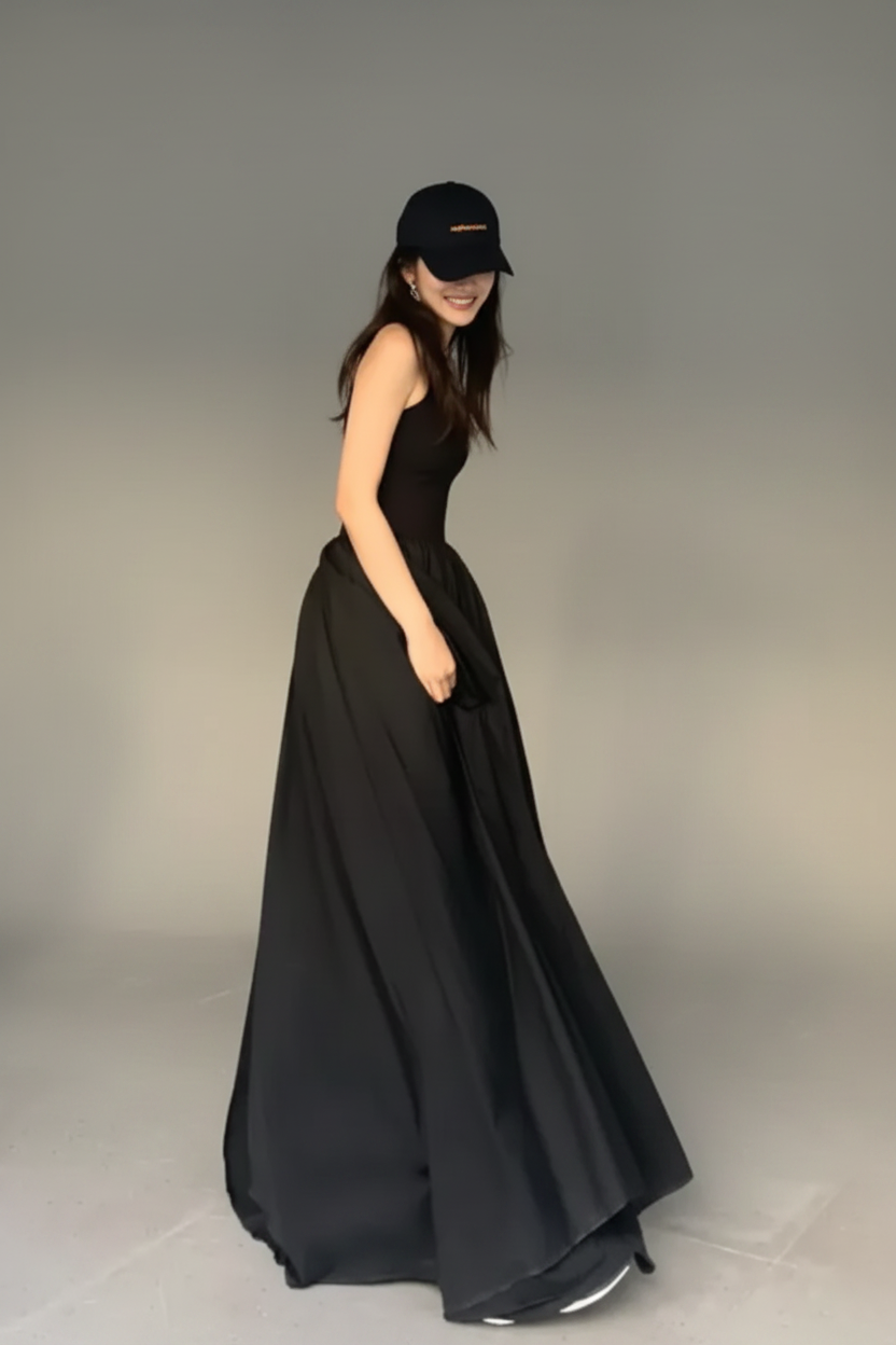Woman in a long black dress and cap standing against a glass block wall.