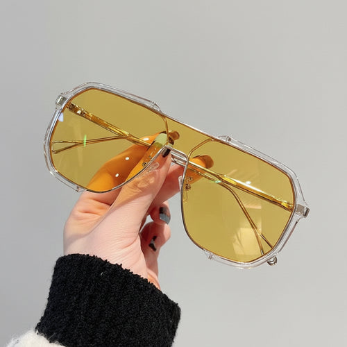 Hand holding a pair of gold-tinted sunglasses against a neutral background