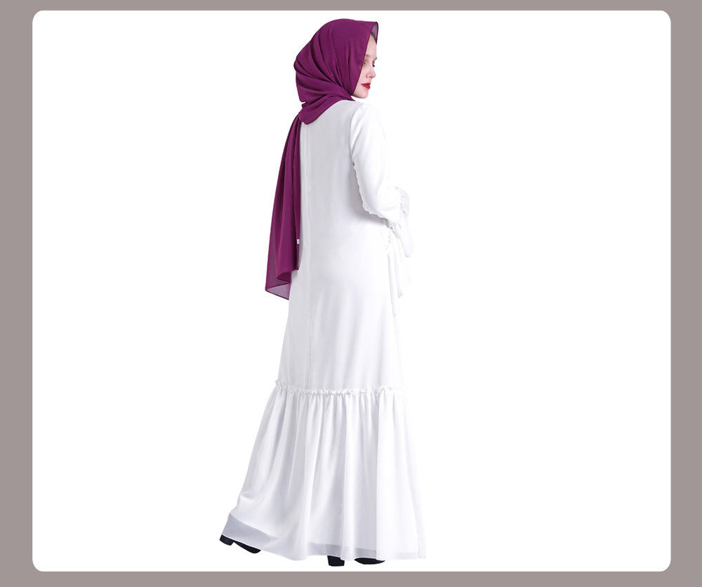 Woman wearing a white dress and purple hijab on a plain background