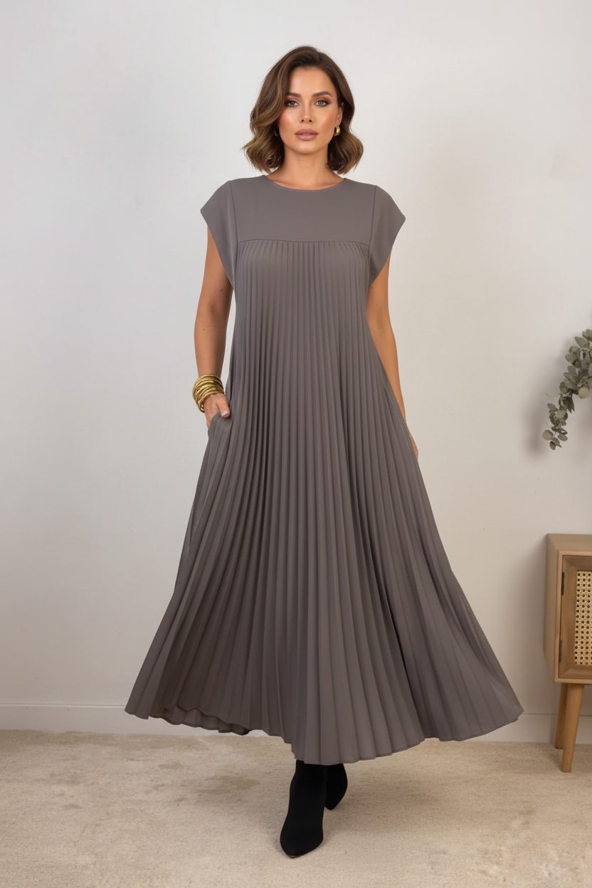 Person wearing a gray pleated dress standing in a room with a white wall and wooden cabinet.