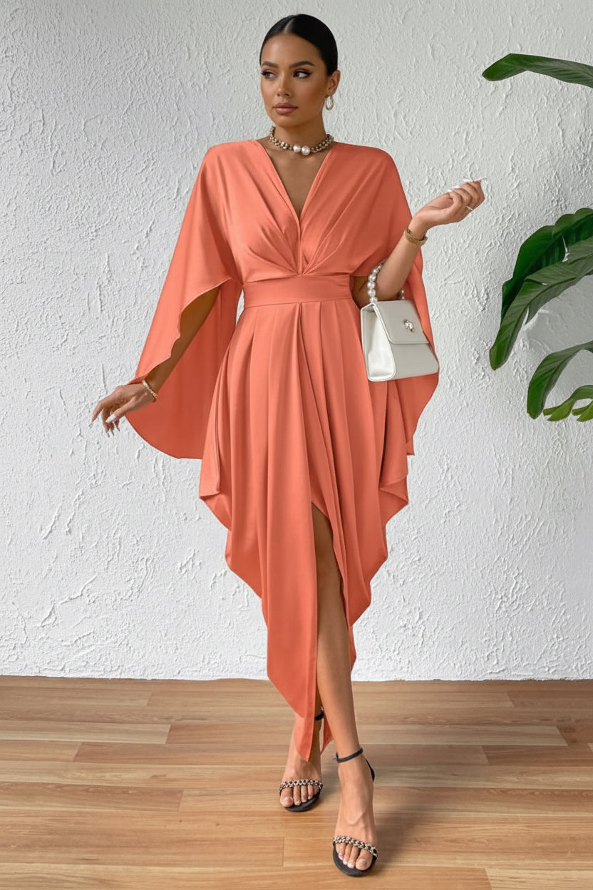 Woman wearing a coral dress with a white wall and plant in the background