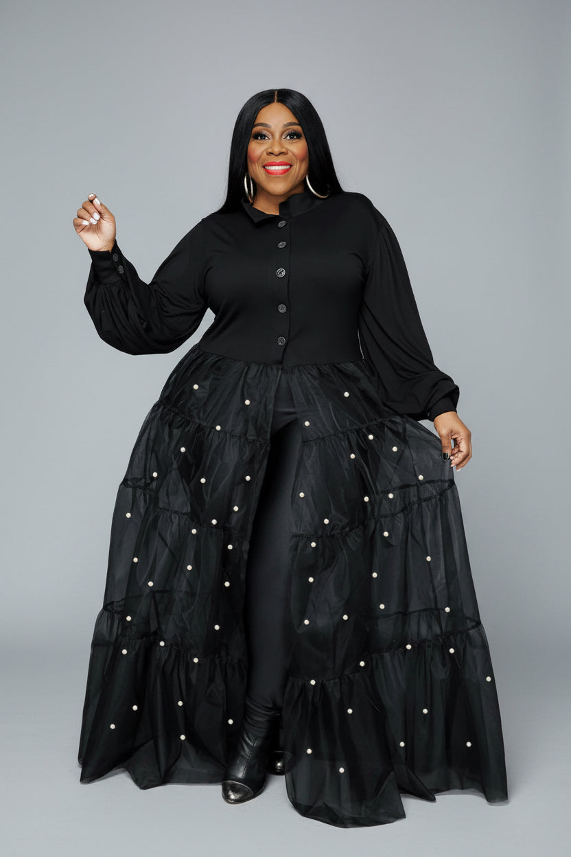Woman wearing a black dress with layered skirt and pearl embellishments outdoors.
