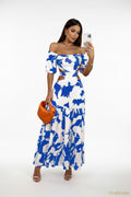Woman wearing a blue and white floral dress holding an orange clutch.