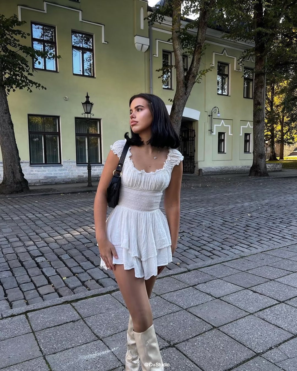 Woman in a white dress standing on a paved street with a building in the background