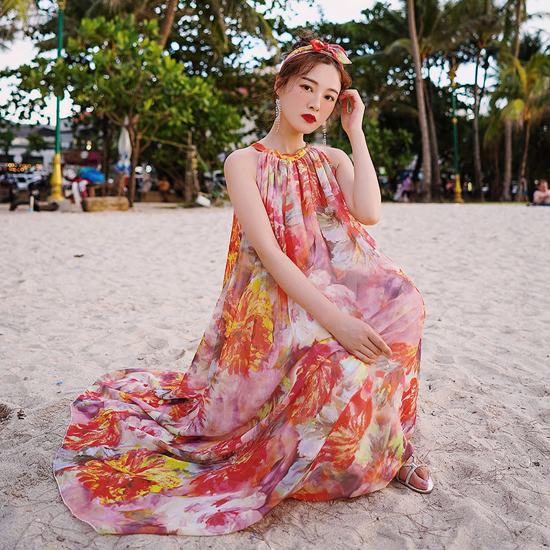 Woman in a colorful floral dress sitting on a sandy beach with palm trees in the background.