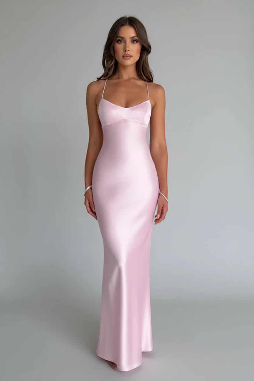 Woman wearing a pink satin dress standing in a minimalistic room with flowers in the background.