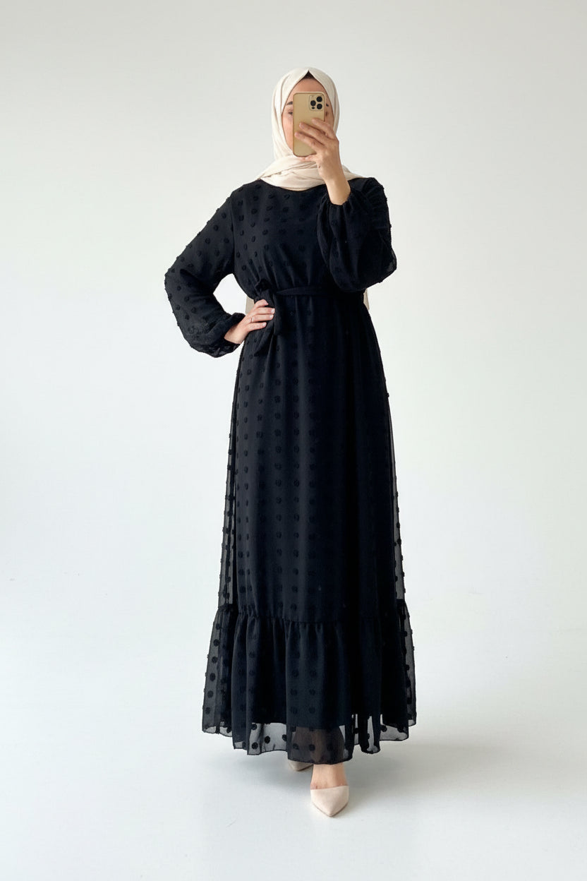 Person wearing a black dress with long sleeves in a bedroom setting.