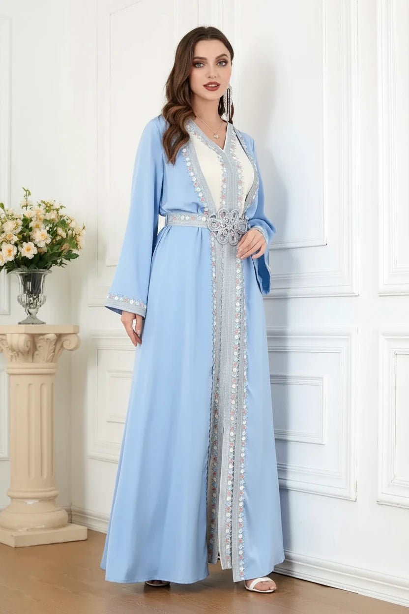 Woman wearing a light blue dress with white embellishments in a room with white walls and a small table with flowers.