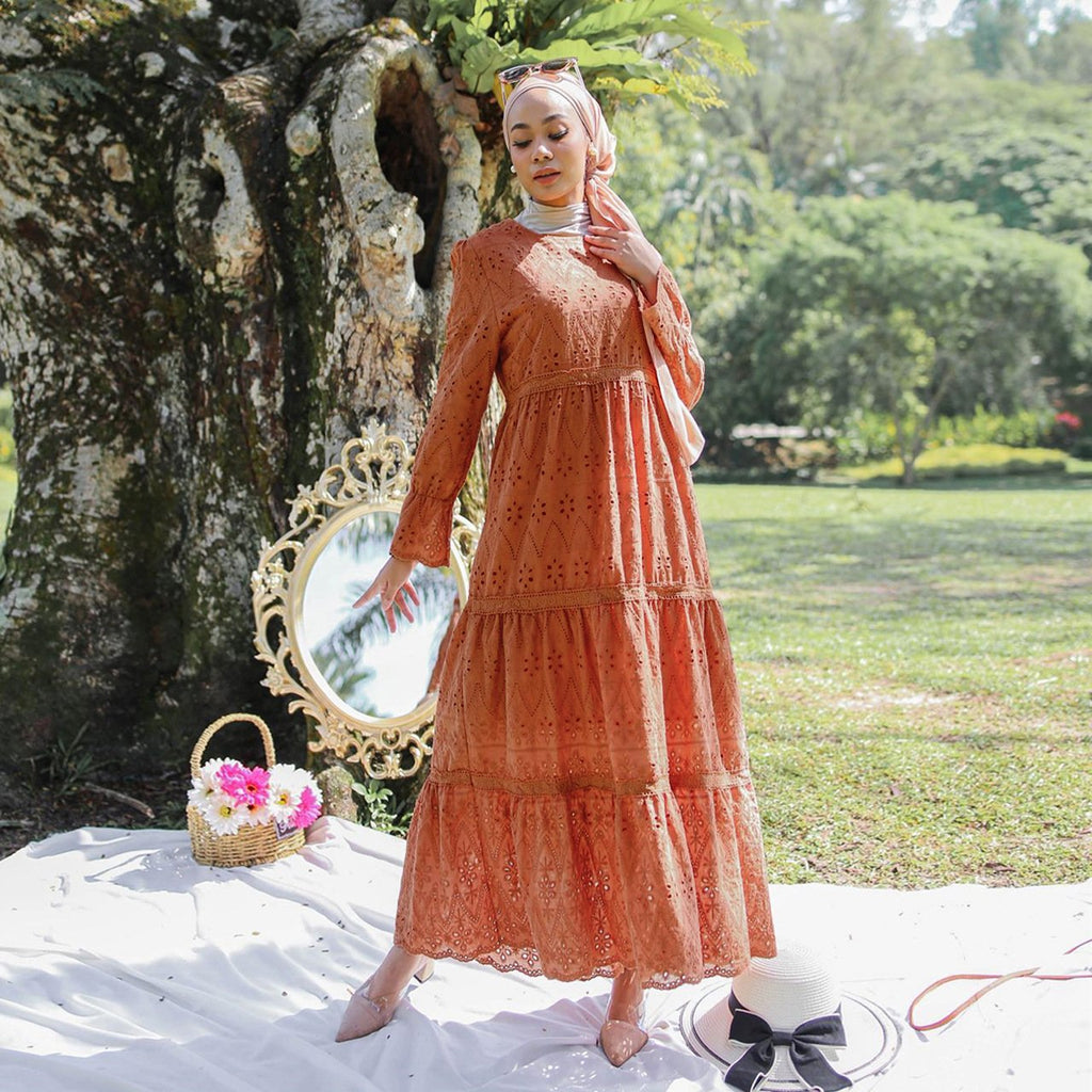 Woman in a long orange dress standing outdoors with a decorative mirror and flowers.