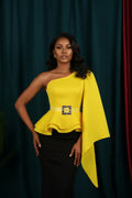 Yellow one-shoulder top with a colorful square design on a mannequin against a dark curtain background.