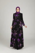 Woman in a black dress with purple floral patterns standing in an elegant indoor setting.
