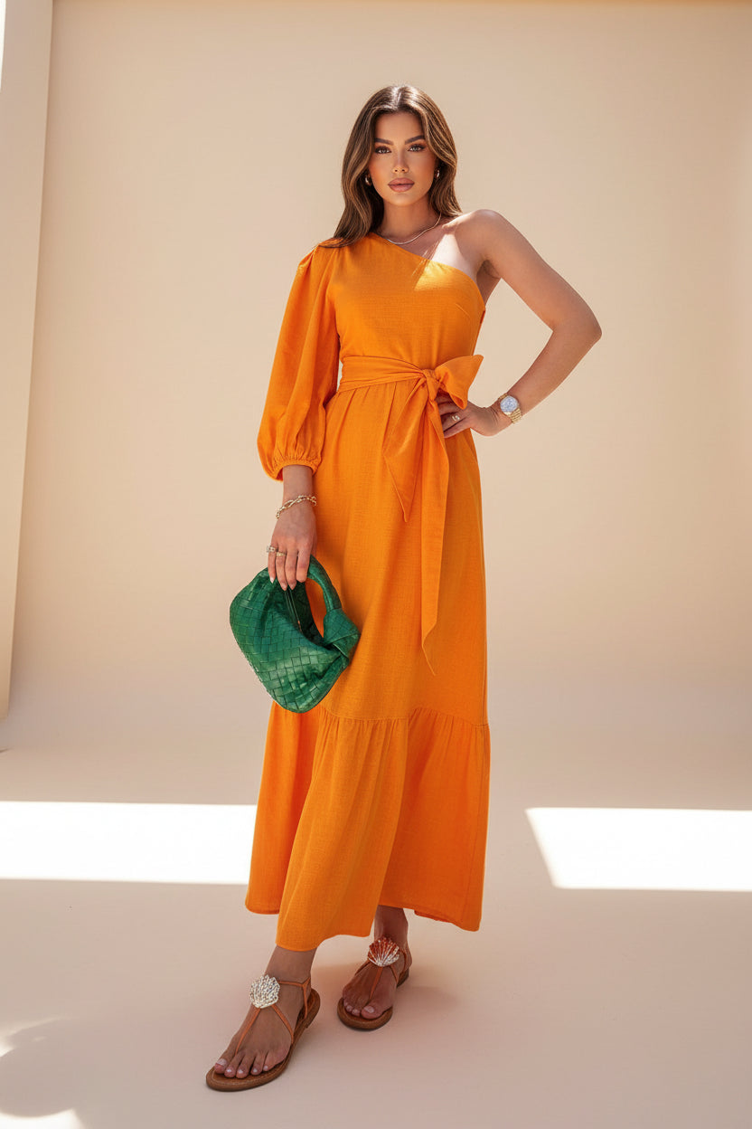 Woman in an orange dress holding a green bag with tropical plants in the background