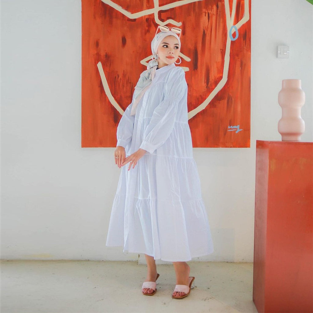 Woman in a white dress standing in a room with abstract art on the wall.