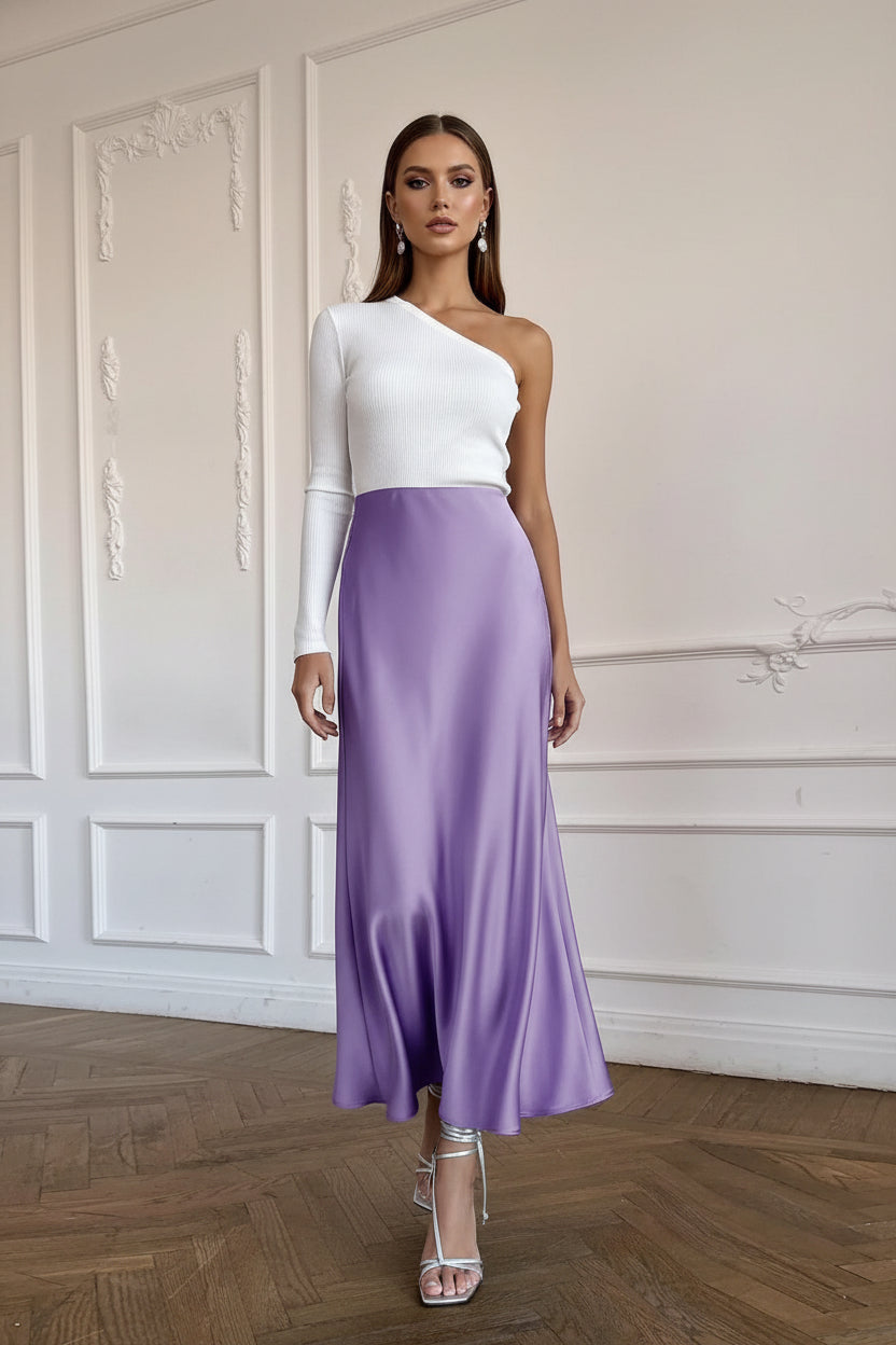 Person wearing a long purple skirt and white top in a room with wooden flooring and white walls.