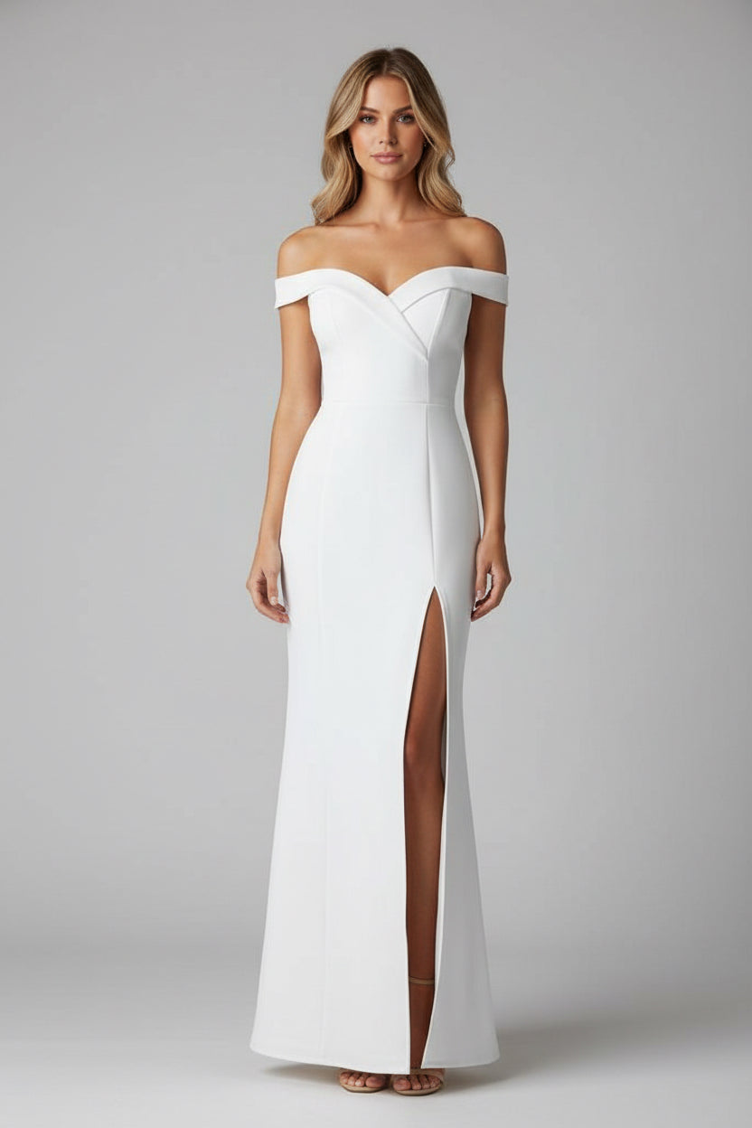 Woman in a white off-shoulder dress with a high slit standing in front of a mirror.