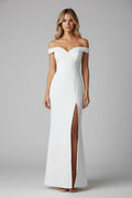 Woman in a white off-shoulder dress with a high slit standing in front of a mirror.