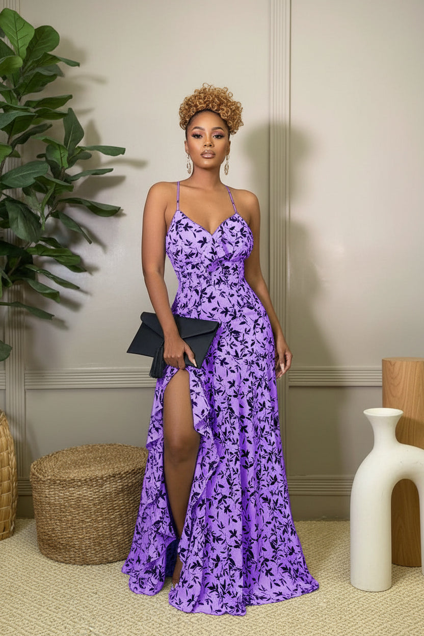 Woman wearing a purple floral dress with a black clutch in an indoor setting.