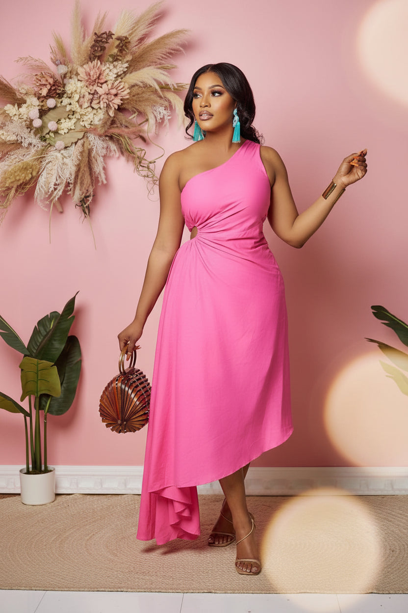 Woman in a pink one-shoulder dress holding a handbag against a pink wall with plants.