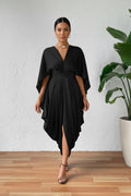 Person wearing a black dress with a draped design on a wooden floor.