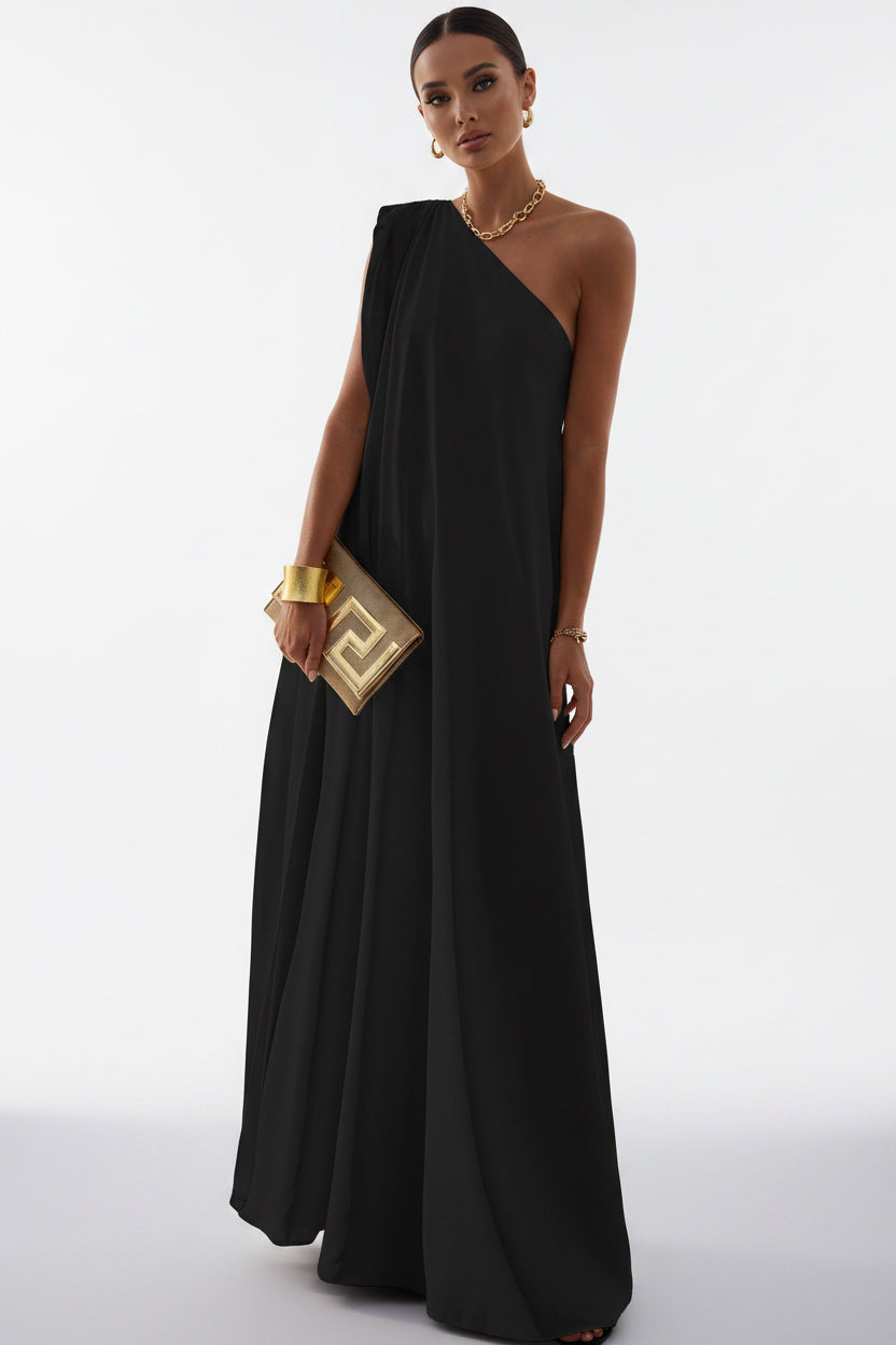 Woman in a black one-shoulder dress holding a gold clutch on a balcony with a scenic view.