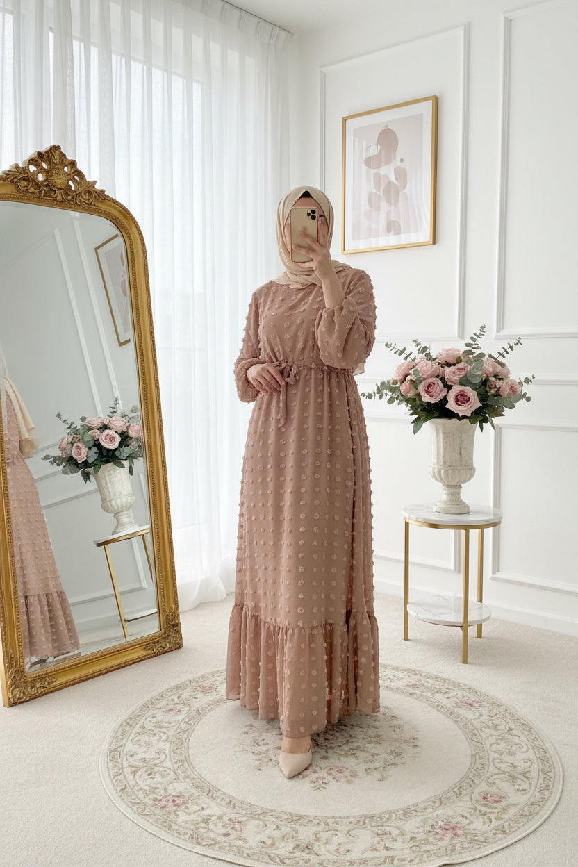 Woman in a long, patterned dress standing in a bedroom with decorative lights and plants.