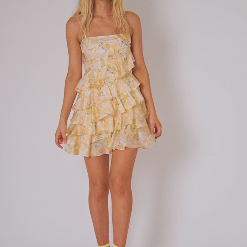 Woman wearing a yellow floral dress against a plain background