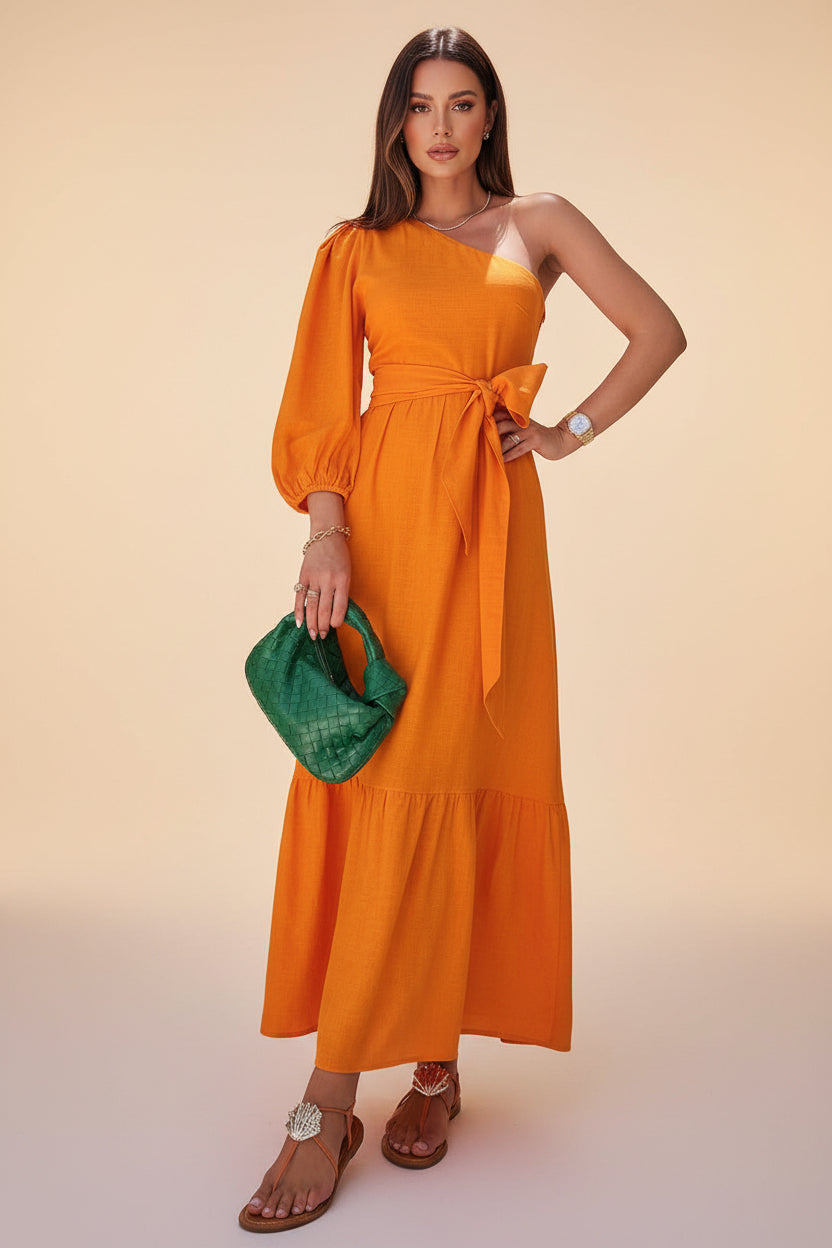 Woman in an orange dress holding a green bag with tropical plants in the background