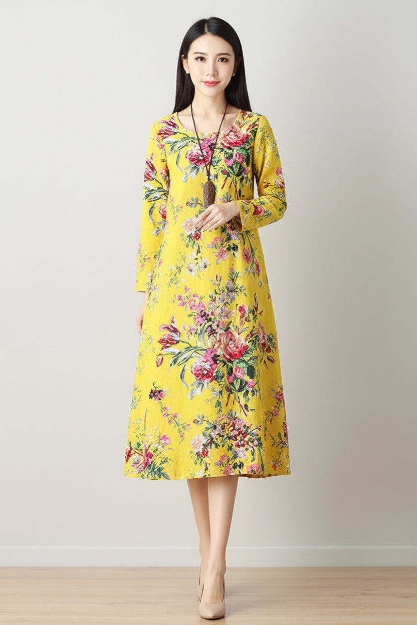 Woman wearing a yellow floral dress holding a beige handbag against a plain background