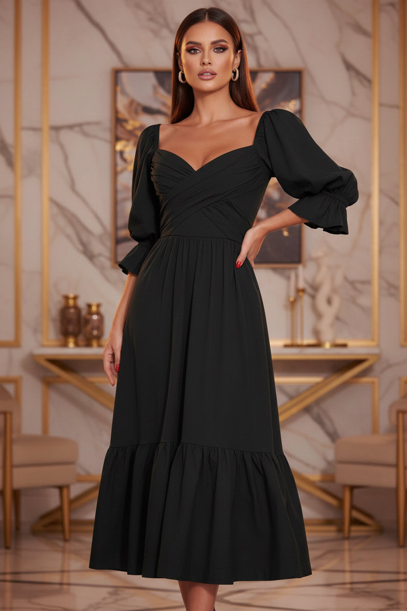 Black dress with puffed sleeves worn by a person standing against a white wall with green foliage.