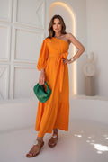 Woman in an orange dress holding a green bag with tropical plants in the background