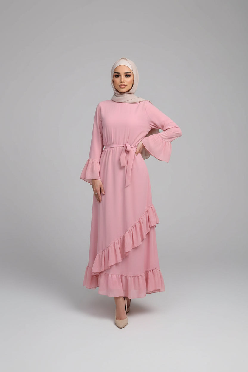 Woman in a pink dress standing outside a building with a brick wall and wooden door.