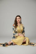 Woman wearing a long, floral-patterned dress with a yellow top sitting on a pink couch.