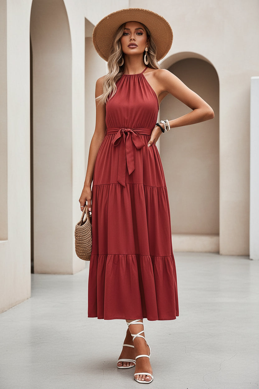 Woman in a red dress sitting on a white wall with a straw bag.