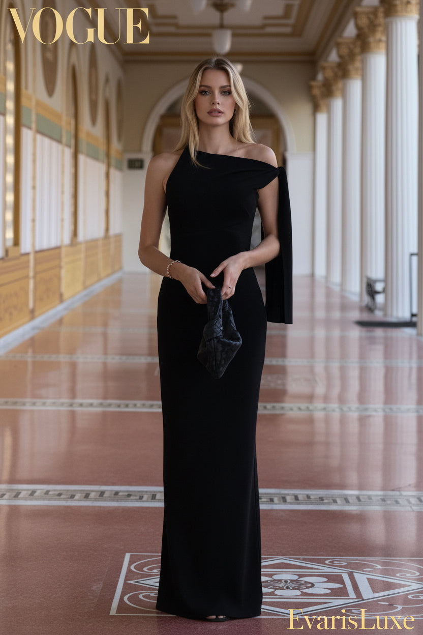 Woman in a black one-shoulder evening gown holding a clutch in an elegant hallway.