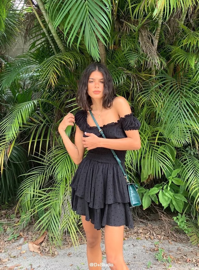Woman in a black dress standing in front of green foliage