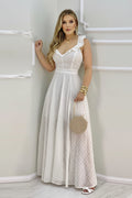 Woman wearing a white polka dot dress holding a round beige handbag against a plain background