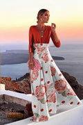 Woman in a floral dress standing on a cliff overlooking the ocean with a cactus plant nearby.