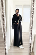Person wearing a black abaya with white trim in front of a decorative mirror.