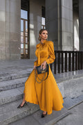 Woman in a mustard yellow dress holding a black handbag on stone steps.