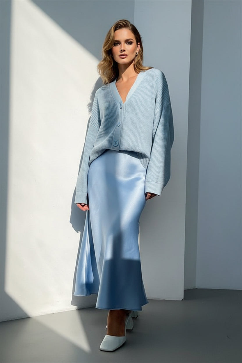 Person wearing a light blue outfit with wide-leg pants and a sweater, standing against a plain wall.
