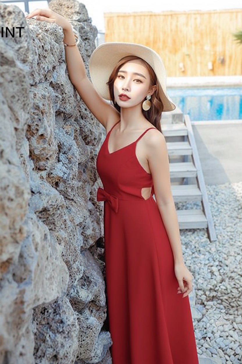 Woman in a red dress and white hat leaning against a stone wall by a pool.