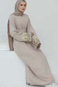 Beige outfit with floral embroidery on sleeves against a white background