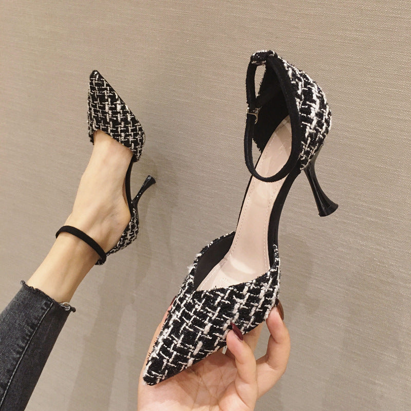 Black and white patterned high-heeled shoes held by a person against a neutral background