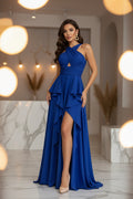 Woman wearing a blue evening gown with a slit, standing against a white wall.