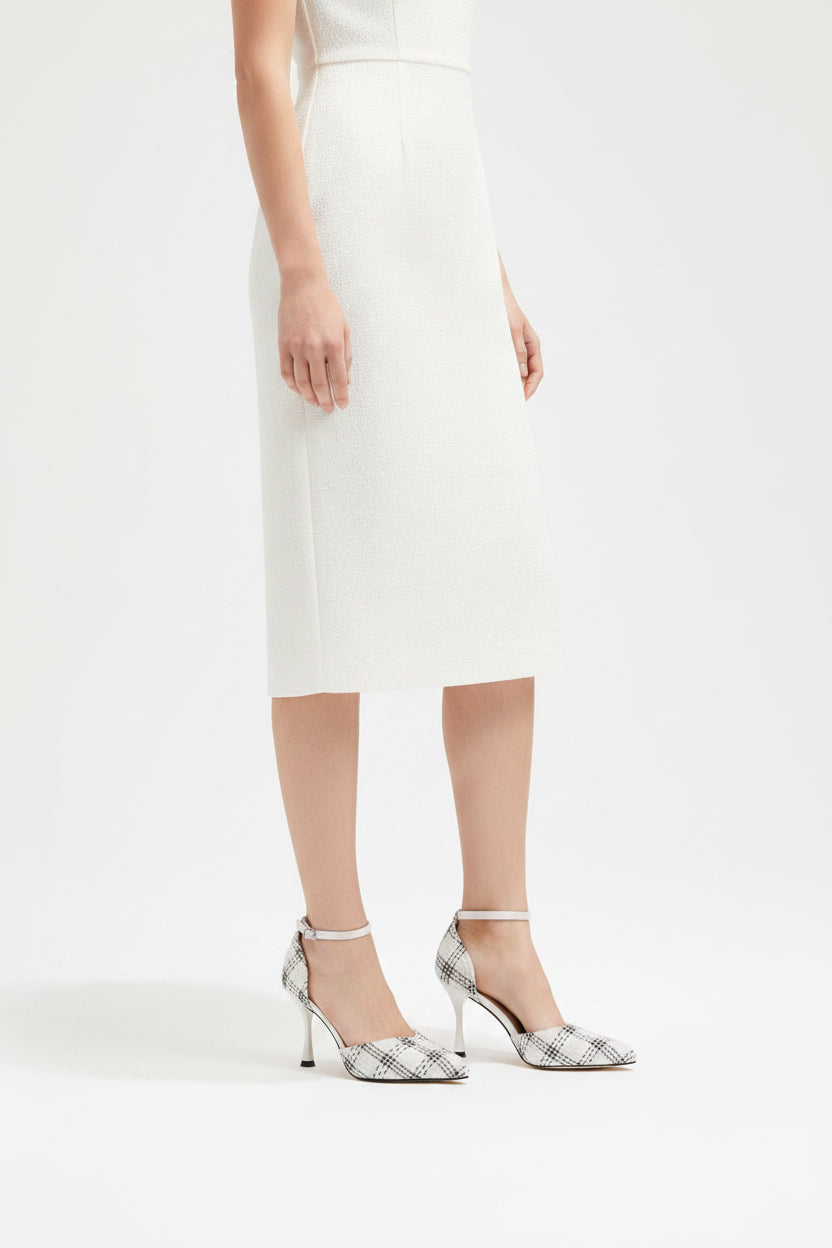White high-heeled shoes with black pattern held by a hand against a neutral background