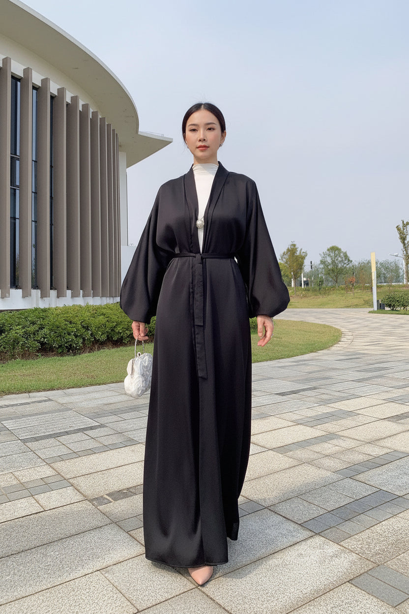 Person wearing a black robe standing on a paved walkway with greenery in the background