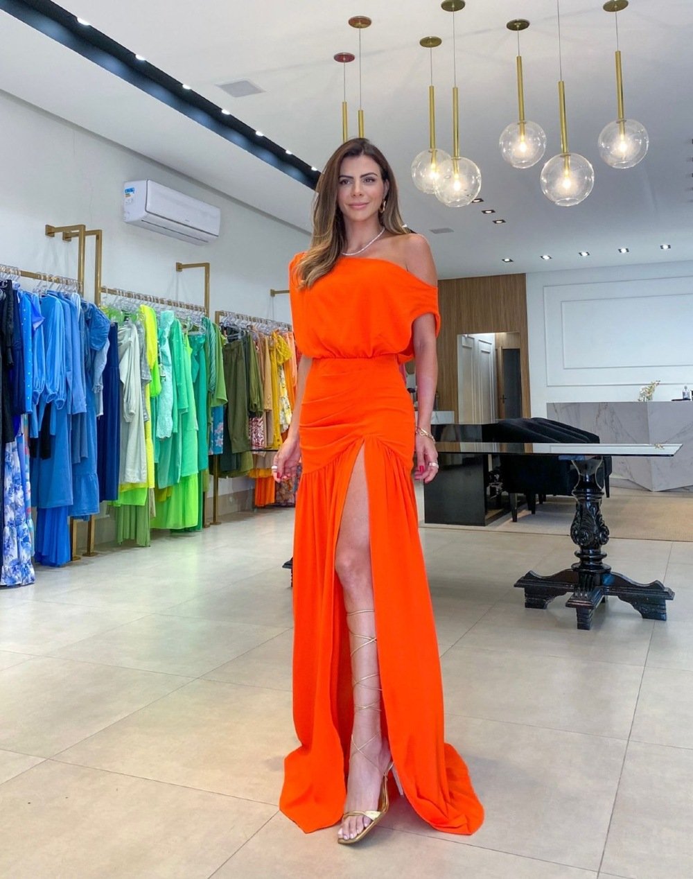 Woman in an orange off-shoulder dress standing in a clothing store.