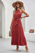 Woman in a red dress sitting on a white wall with a straw bag.